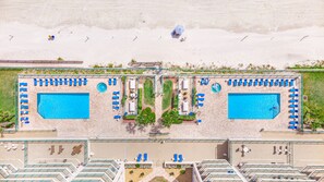 Eine Luftaufnahme eines Resorts mit zwei Swimmingpools, Liegestühlen und einem Strandabschnitt.