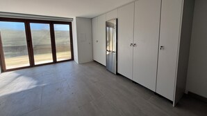 Una habitación amplia con un gran ventanal corredera que da a un balcón, un armario empotrado y un refrigerador de acero inoxidable.