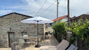 Un edificio de piedra con un patio, mobiliario exterior y una pérgola con sombrilla.