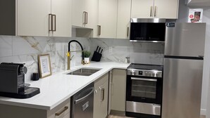 Una cocina moderna con armarios blancos, electrodomésticos de acero inoxidable, horno empotrado y refrigerador.