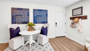 Una sala de estar moderna con un sofá blanco, dos piezas de arte mural azul con estampado, una mesa redonda blanca con una planta y piso de madera.
