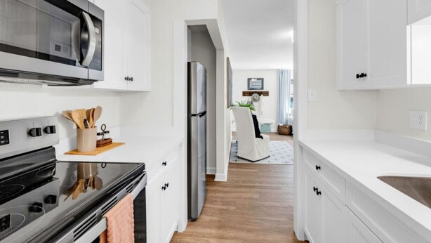 Una cocina moderna con armarios blancos, electrodomésticos de acero inoxidable y piso de madera.