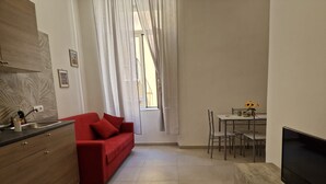 Un espace de vie compact comprenant un coin cuisine, un canapé rouge, un coin repas avec une table et des chaises, et un téléviseur posé sur un meuble en bois.