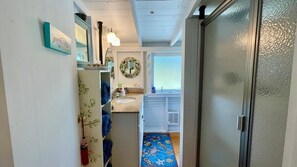 A narrow hallway leading to a bathroom with a sink, mirror, and a blue patterned rug.