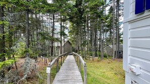 Un sentier en bois mène à un chalet entouré de grands arbres.