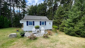 Une petite maison avec un patio en pierre, deux fauteuils Adirondack et une plante en pot.