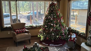 Un salón acogedor con un gran árbol de Navidad, un sillón cómodo y una mesita con un centro de mesa decorativo.