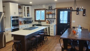 Una cocina moderna con electrodomésticos de acero inoxidable, una isla central con taburetes y una zona de comedor con mesa y sillas de madera.