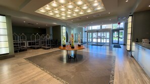A spacious lobby with a central round table, a ceiling with recessed lighting, and a view of the outside through glass doors.