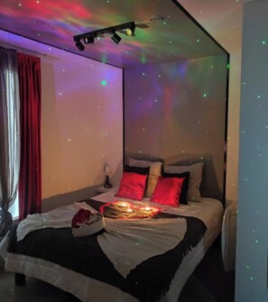 A modern bedroom with a bed, red and white bedding, a ceiling projector, and a starry night effect. - Beautiful apartment in Tours center, panoramic view of the city. (Tours)