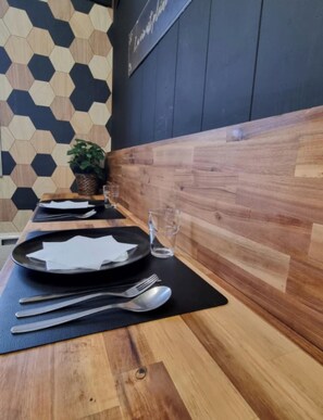 A dining table set with plates, cutlery, and glasses, with a wooden wall and a geometric pattern in the background. - Beautiful apartment in Tours center, panoramic view of the city. (Tours)