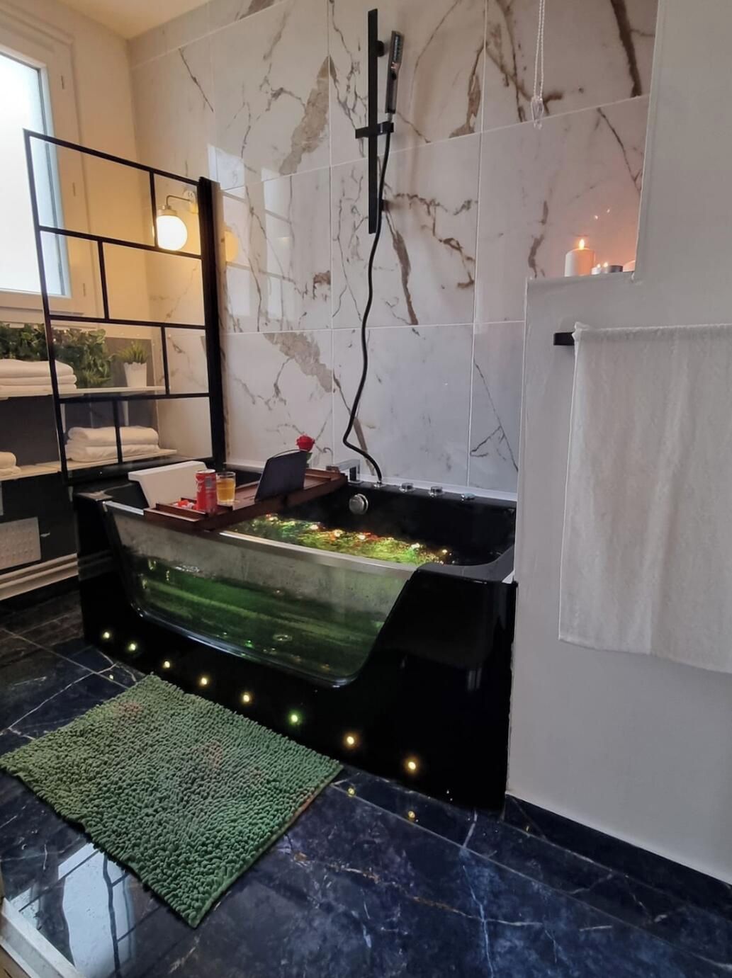 A modern bathroom with a freestanding bathtub, marble tiles, a green rug, and a towel rack.