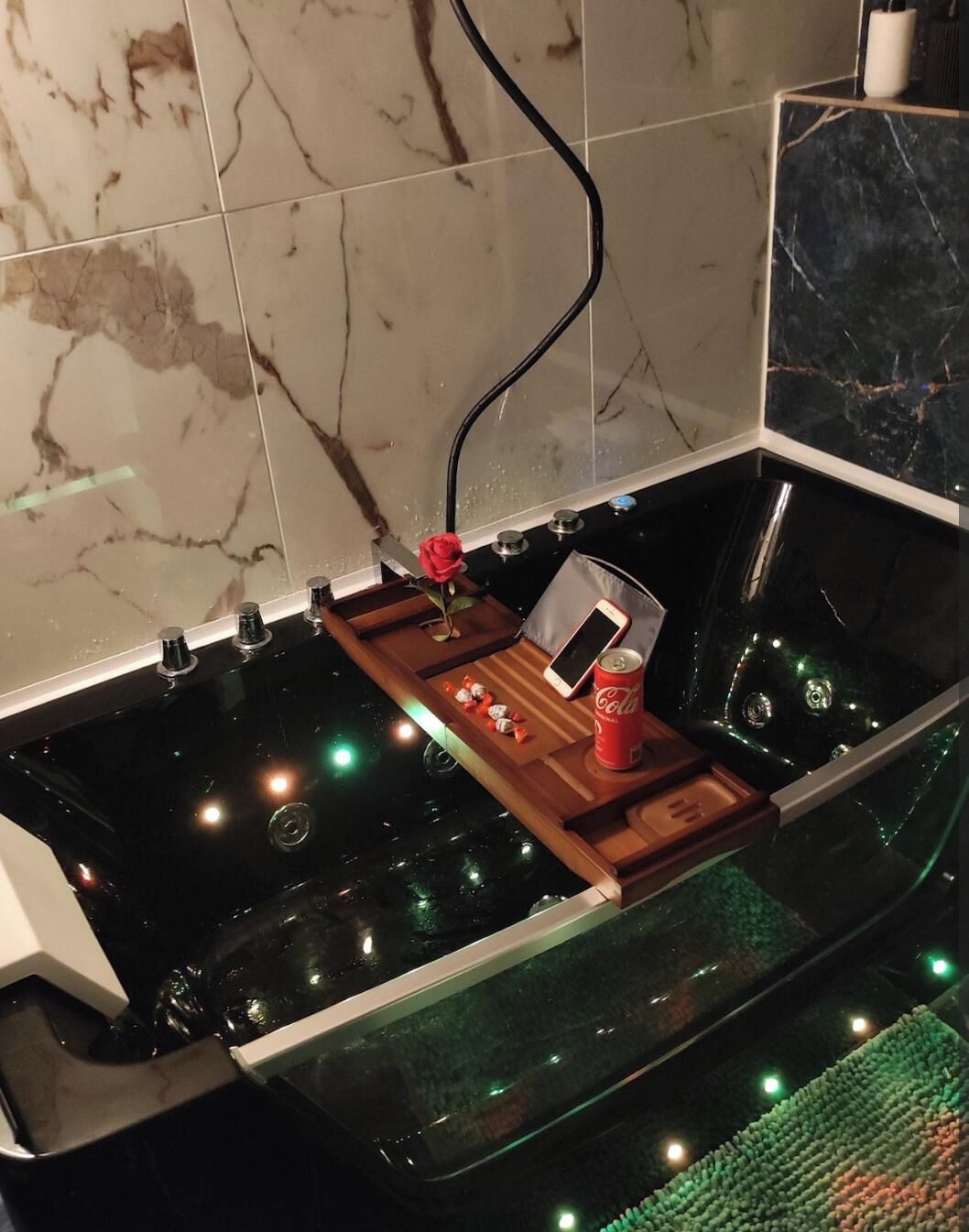Une baignoire avec un plateau en bois, une rose, un téléphone intelligent et une canette de Coca-Cola.