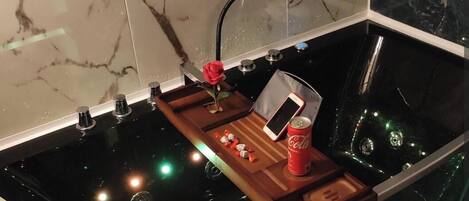 A bathtub with a wooden tray, a rose, a smartphone, and a can of Coca-Cola.