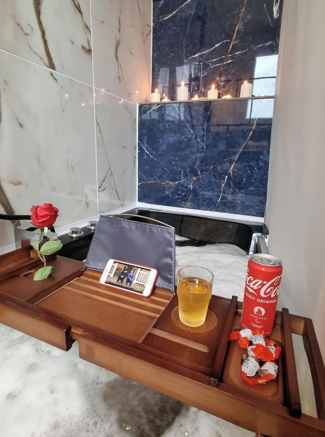 Un tavolo di legno con una rosa, uno smartphone, una tazza di tè, una lattina di Coca-Cola e cioccolatini.