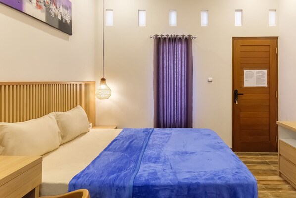 A bedroom with a bed, a nightstand, a wooden headboard, a hanging light fixture, a door with a sign, and a window with curtains.