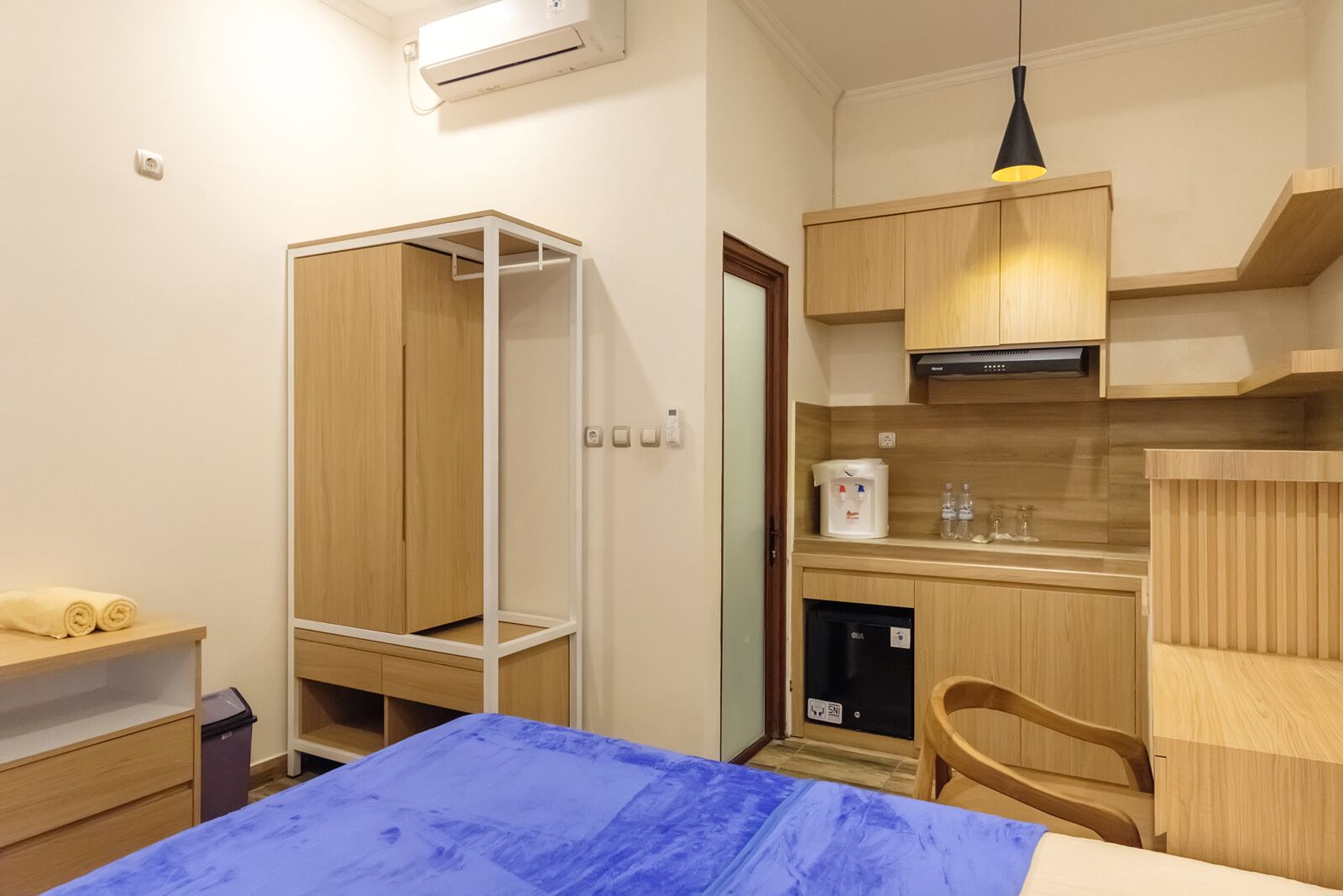 Ein kleines Hotelzimmer mit Bett, Schreibtisch, Küchenzeile und Kleiderschrank.