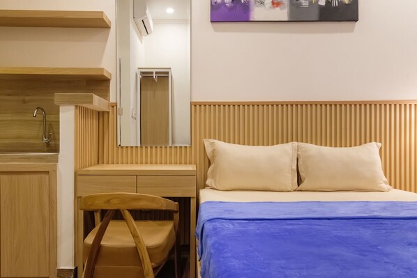 Une chambre d’hôtel avec un bureau en bois, une chaise, un lit recouvert d’une courtepointe bleue et un miroir fixé au mur.
