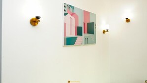 Ein schlicht eingerichteter Raum mit einem einzelnen abstrakten Gemälde an der Wand, zwei Wandleuchten und einem sichtbaren Logo unten.