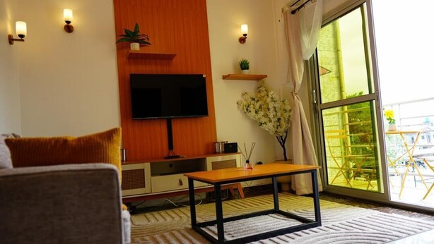Ein modernes Wohnzimmer mit Flachbildfernseher, Holzregalen, einem kleinen Tisch und einem großen Fenster mit Blick nach draußen.
