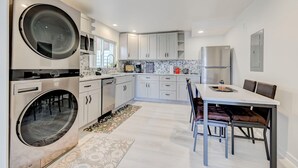 Une cuisine moderne dotée d’appareils électroménagers intégrés, un coin repas avec une table et des chaises, et un grand lave-linge.