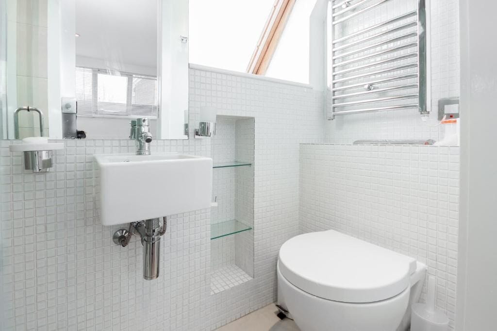 Un baño moderno con lavamanos blanco, cabina de ducha con mampara de vidrio y un inodoro blanco.