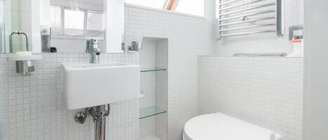 Un baño moderno con lavamanos blanco, cabina de ducha con mampara de vidrio y un inodoro blanco.