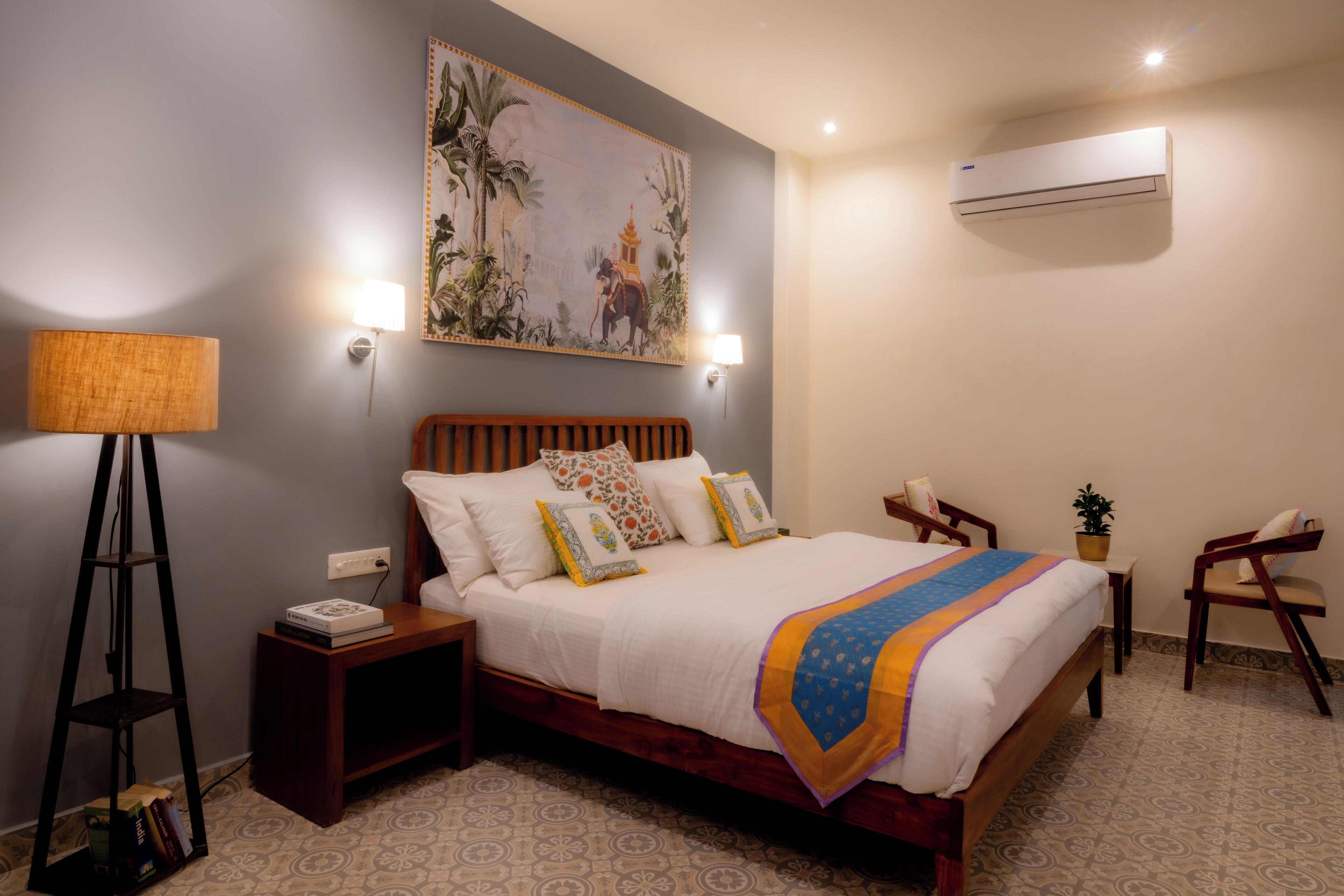 Une chambre à coucher bien rangée, avec un lit, des tables de chevet, une lampe, un climatiseur fixé au mur et un tableau.