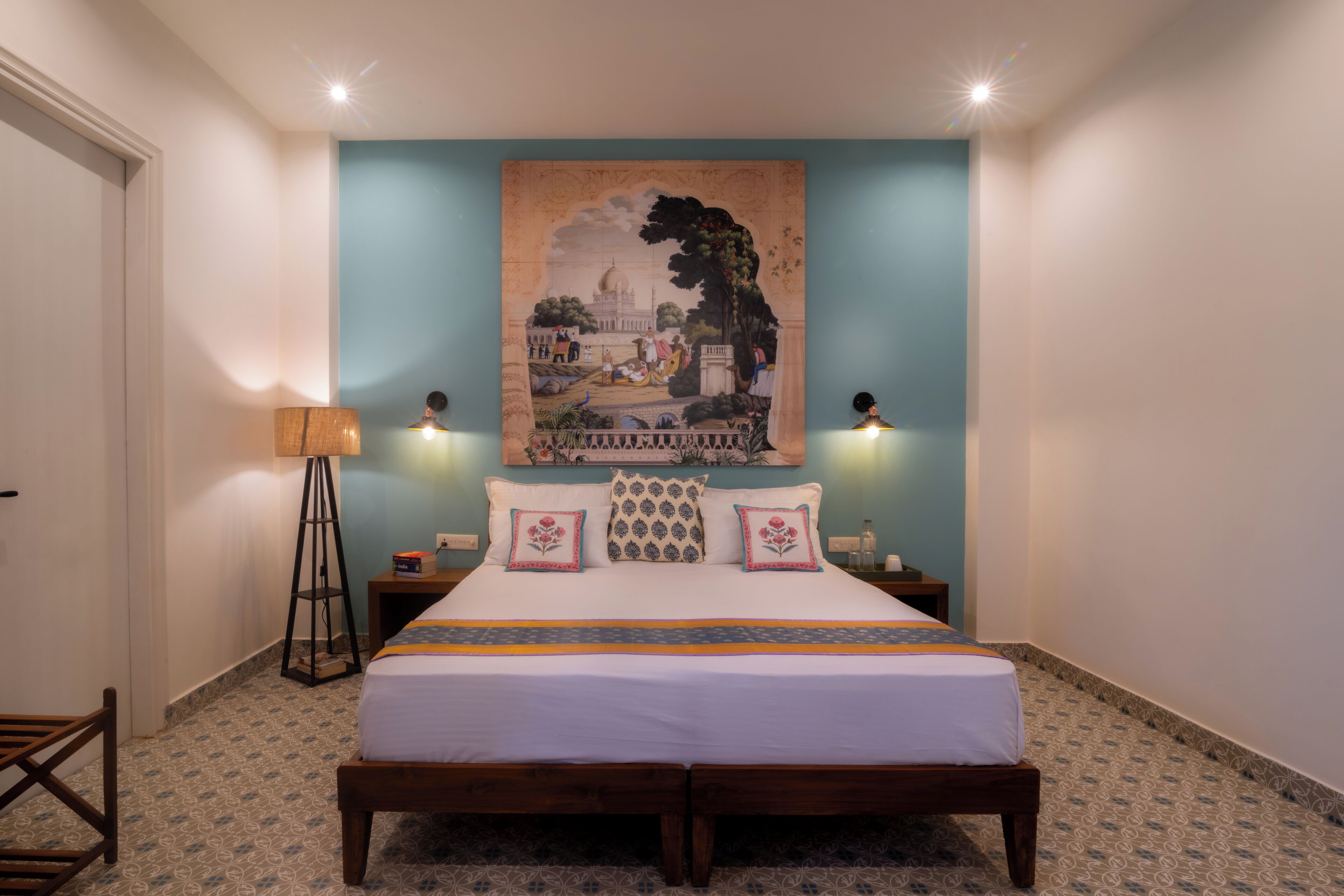 Een slaapkamer met een bed, twee nachtkastjes, een vloerlamp en een aan de muur hangend schilderij.
