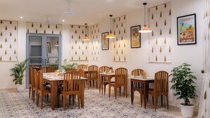A dining area with wooden tables and chairs, patterned floor tiles, pendant lighting, and wall decorations. - Inara House (Agra)