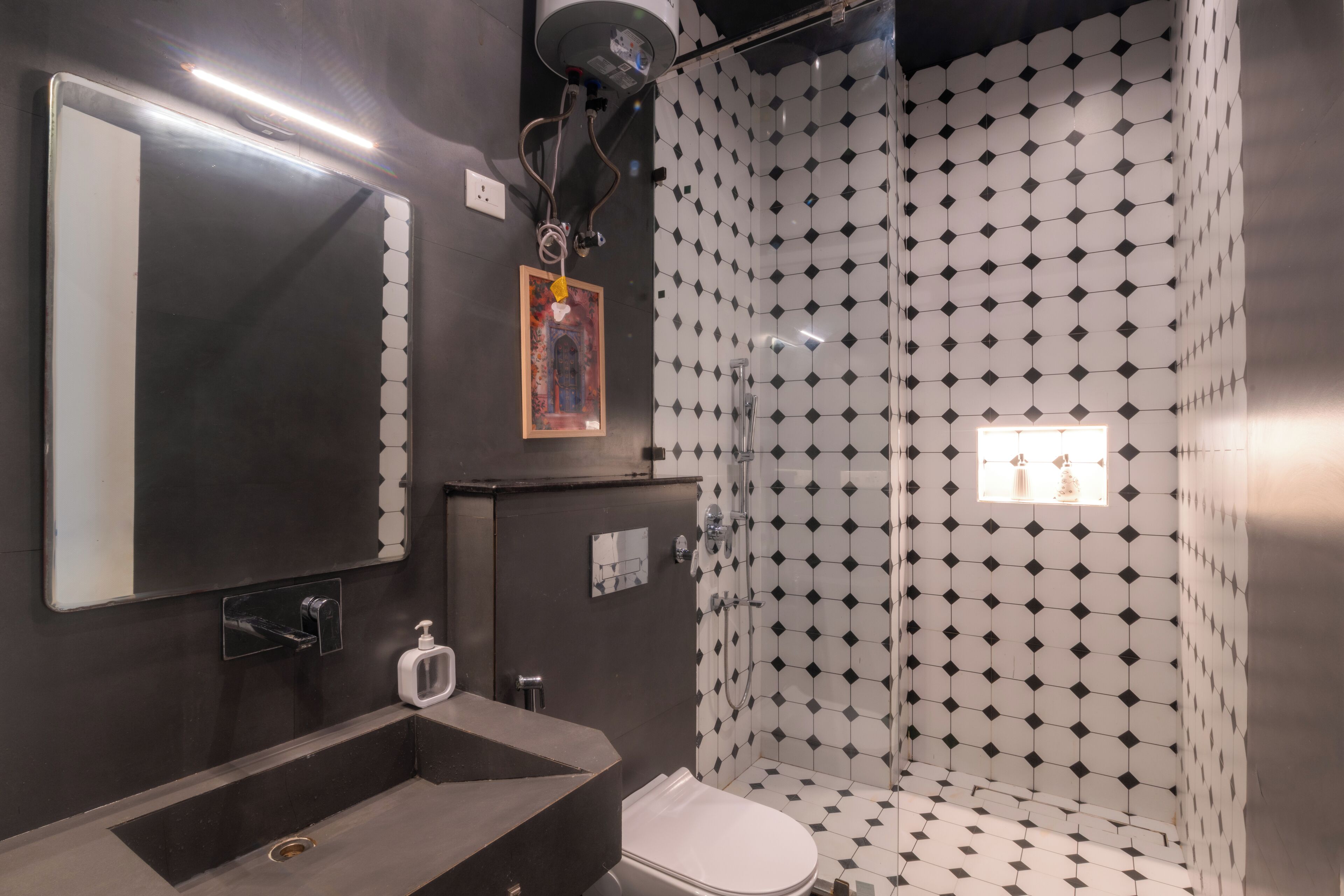 Un baño moderno con un espejo grande, un lavamanos, un inodoro y una ducha con un diseño de mosaicos geométricos.