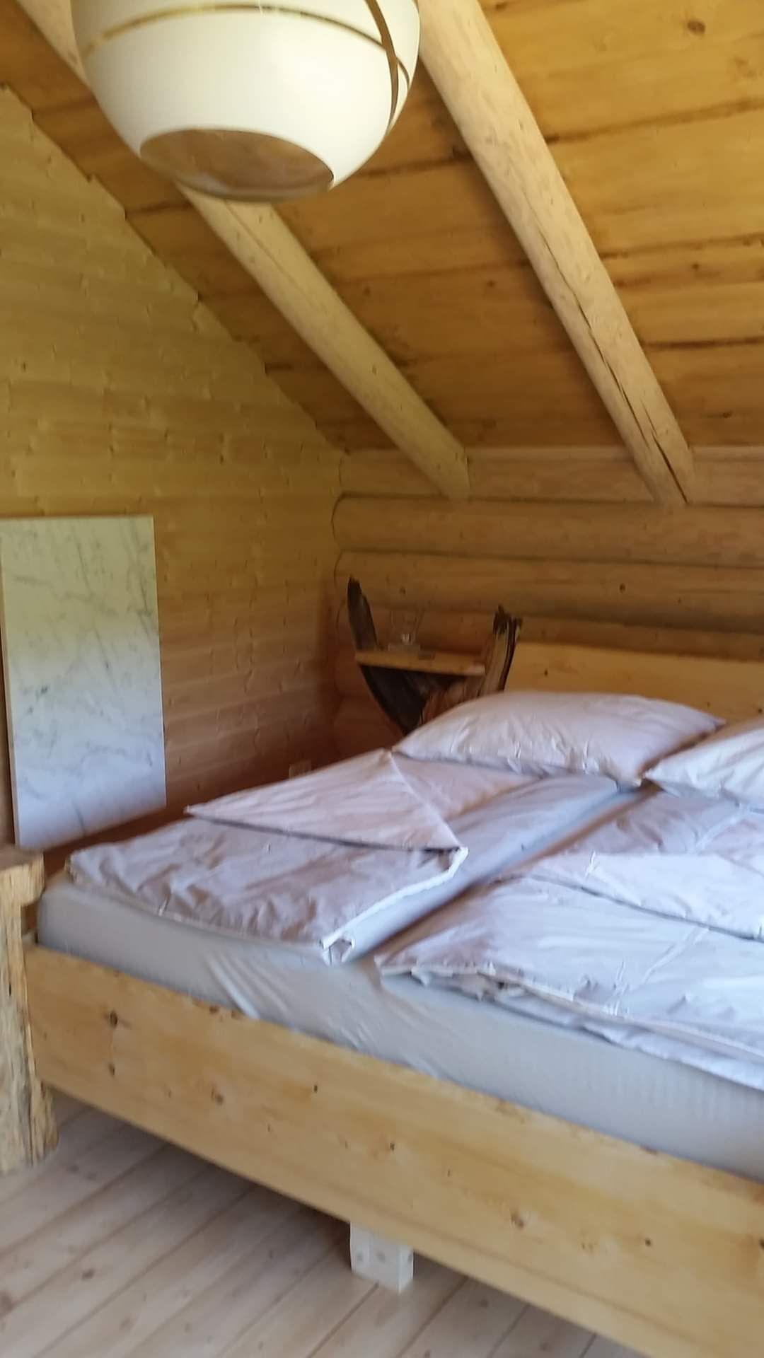 A wooden cabin interior with a bed, a slanted ceiling, and a wooden floor.