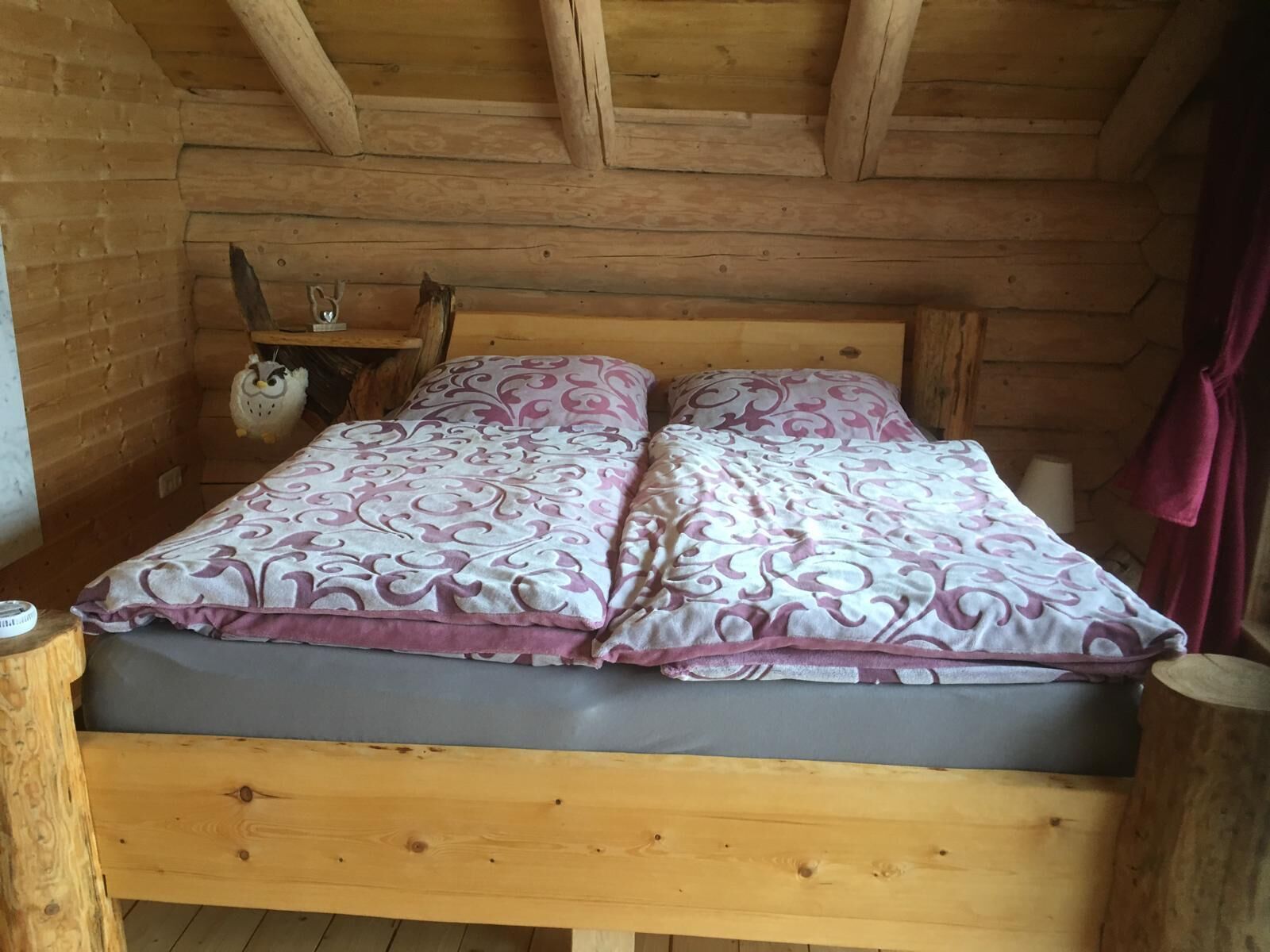 A wooden cabin bedroom with a bed, pillows, a nightstand, and a shelf with a decorative owl.