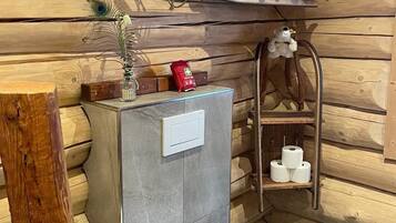 A compact bathroom with a toilet, a shelf with toiletries, and a wooden bench.