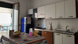 Une cuisine compacte avec des meubles blancs, un réfrigérateur bleu, une nappe à rayures et un coin repas avec des chaises.