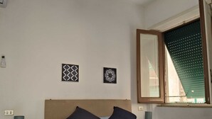 Une chambre à coucher comprenant un lit, deux oreillers, une table de chevet avec une lampe, une prise de courant murale et deux éléments décoratifs fixés au mur.