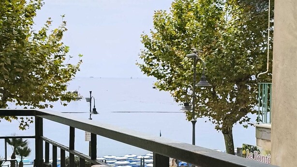 Un balcon avec vue sur la mer, agrémenté d’une table où sont disposées des boissons et des fruits, et d’une enseigne indiquant « Le Bontà ».