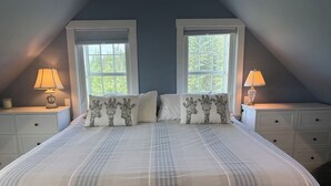 A bedroom with a large bed, two windows, a nightstand with a lamp, and a dresser.