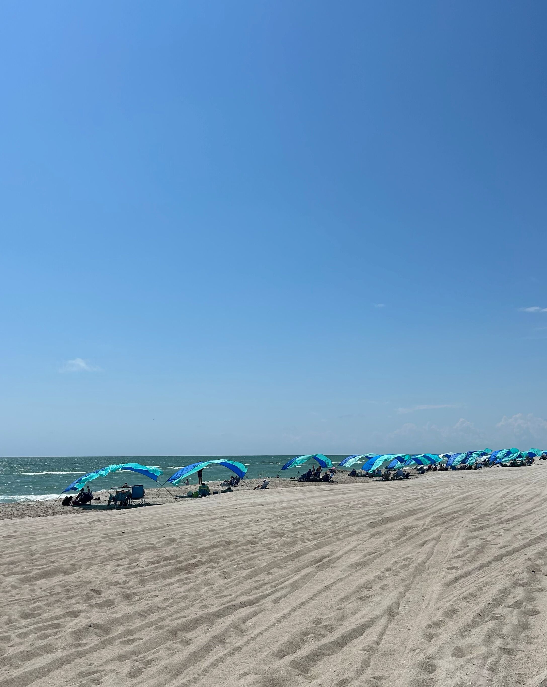 En sandstrand med rader av blåa strandparasoller och stolar.