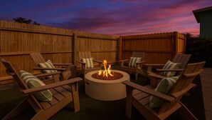 A patio area with a circular fire pit surrounded by wooden chairs with striped cushions. - One Last Summer Family Escape Pool• Arcade• Games (Bradenton)