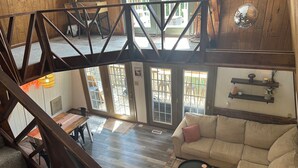 A spacious living area with a high ceiling, wooden beams, a staircase, a dining area, and a view through large glass doors. - Charming A-frame with Lake Cumberland Views (Jamestown)