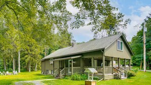 A single-story cabin with a porch, surrounded by a grassy yard and trees. - Private Cottage Close to Shopping, Skiing, Swimming, Hiking, Biking and Dining. (Austerlitz)