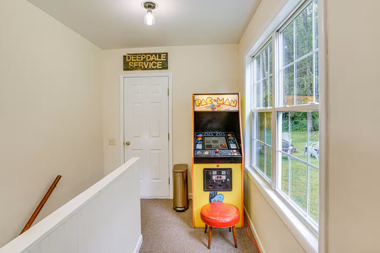 A hallway with a Pac-Man arcade machine, a door labeled 'Deepdale Service,' and a window with a view of greenery.
