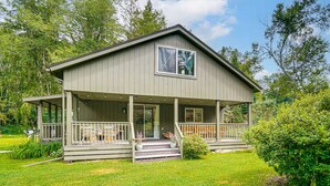 A two-story house with a porch, a covered deck, and a large window. - Private Cottage Close to Shopping, Skiing, Swimming, Hiking, Biking and Dining. (Austerlitz)