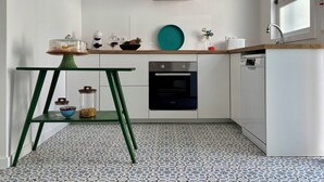 Une cuisine compacte avec des meubles blancs, un four encastré, un lave-vaisselle et une table en métal vert.