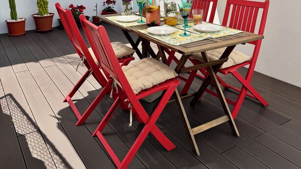 Une terrasse extérieure avec une table dressée pour le repas, entourée de chaises rouges, sous un grand parasol.