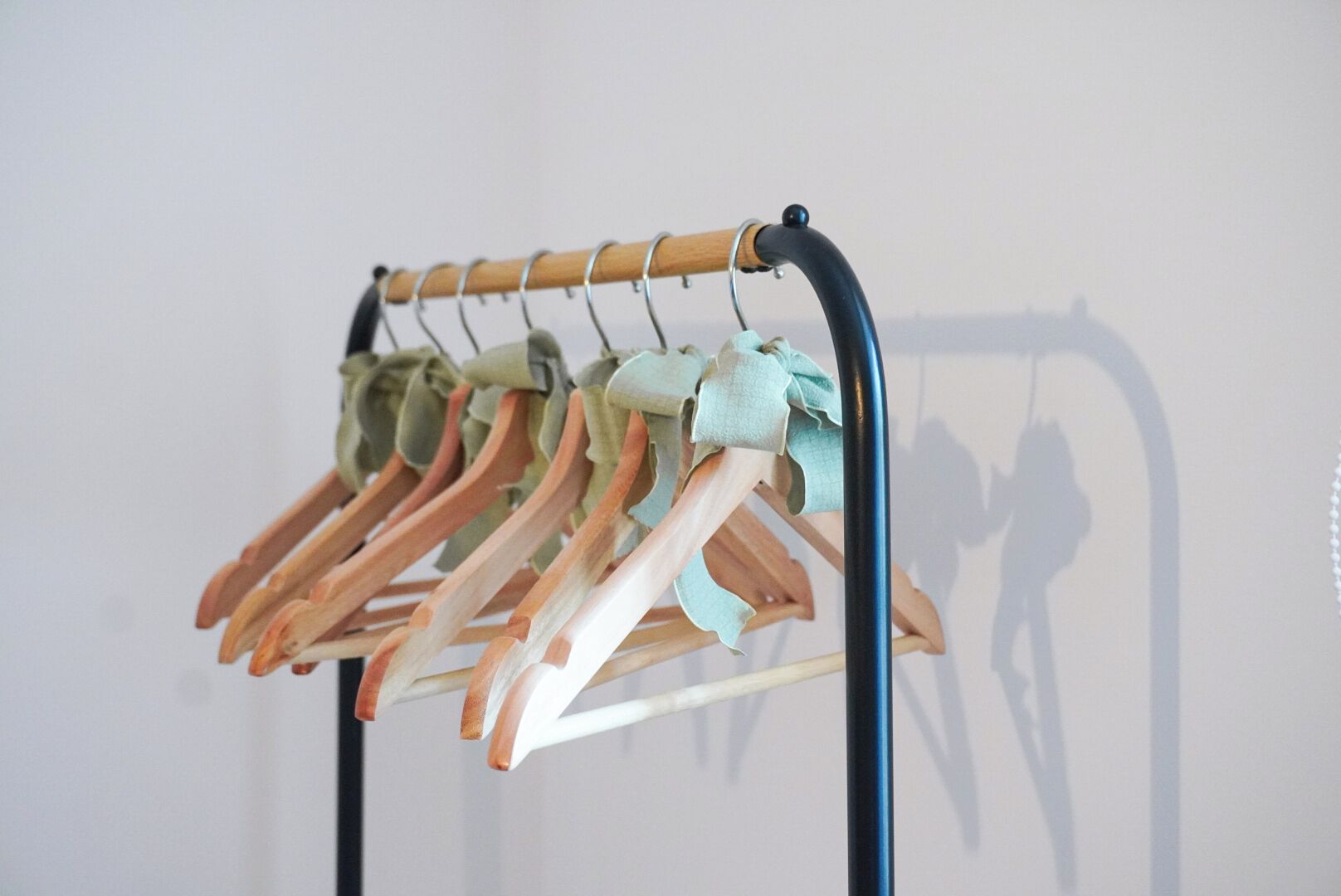 Een kledingrek met meerdere houten hangers, waarvan sommige bekleed zijn, voor een effen achtergrond.