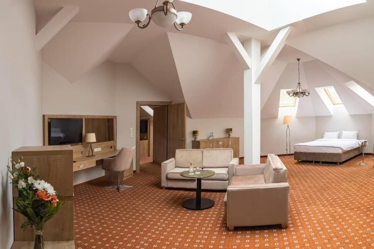 A spacious room with a high ceiling, a sofa, a coffee table, a TV, a bed, and a desk with a lamp.
