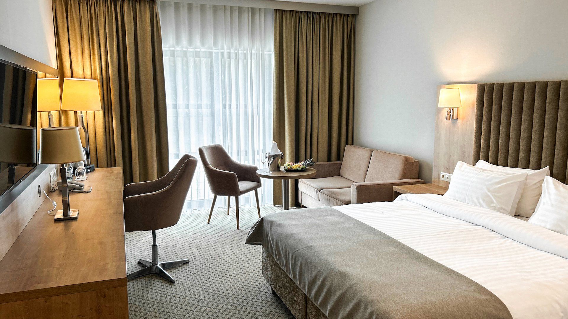 Una habitación de hotel con cama, escritorio, dos sillas, una mesita y televisor.