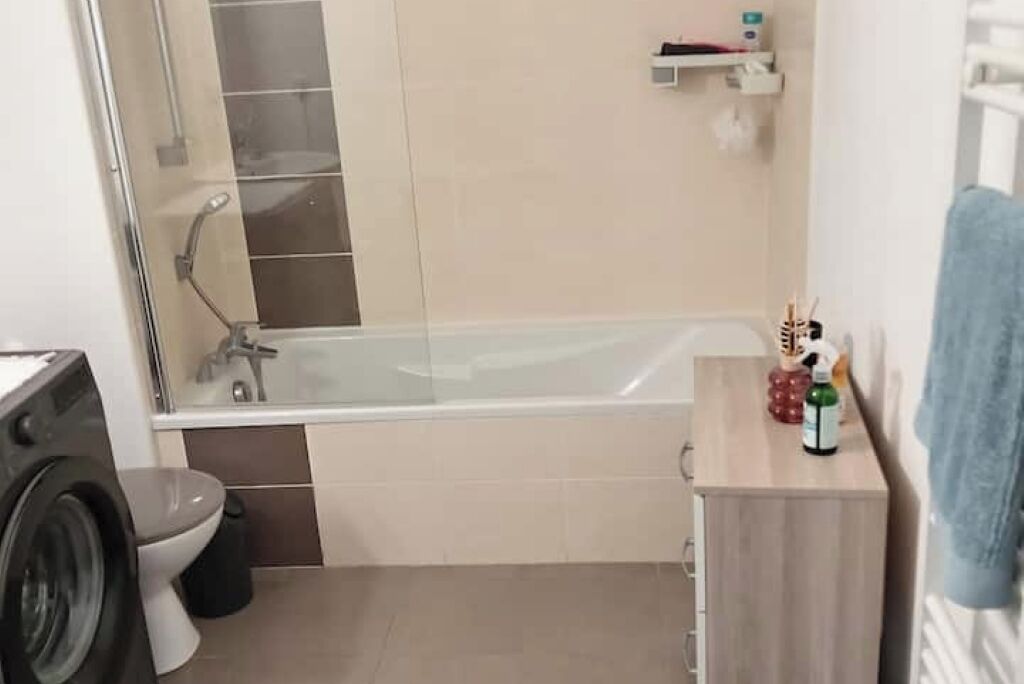 A compact bathroom with a glass-enclosed shower, a toilet, and a washing machine.